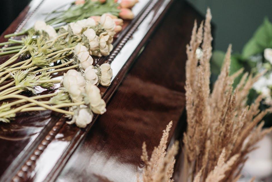 A close-up of a floral arrangement featuring white garden roses and pale pink tulips laid on a polished dark wooden surface, with some greenery visible in the background. The flowers are arranged in a