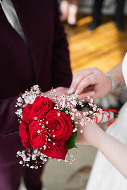 A bouquet of vibrant red roses, accented with delicate white baby's breath, is being handed over during a floral arrangement or gift exchange at a wedding event. The bouquet features fresh, velvety pe